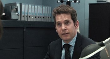 Movie still from “In the Loop” (2009), directed by Armando Iannucci – A man wearing a suit and tie in an office setting; Close Up shot, Over the shoulder angle