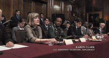 Movie still from “In the Loop” (2009), directed by Armando Iannucci – A group of people sitting around a table; Medium shot, Over the shoulder angle
