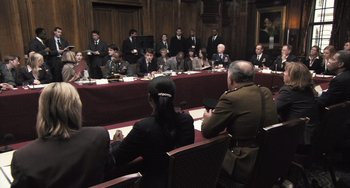 Movie still from “In the Loop” (2009), directed by Armando Iannucci – A group of men and women sitting at a table in front of each other; Wide shot, High angle