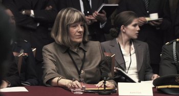 Movie still from “In the Loop” (2009), directed by Armando Iannucci – A woman sitting at a table in front of a microphone; Close Up shot, Over the shoulder angle
