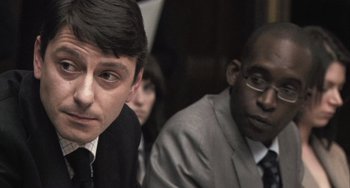Movie still from “In the Loop” (2009), directed by Armando Iannucci – Two men and a woman are sitting in a room; Close Up shot, Over the shoulder angle