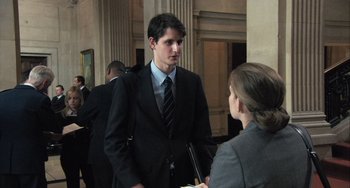 Movie still from “In the Loop” (2009), directed by Armando Iannucci – A man in a business suit talking to a woman in a business suit; Medium shot, Low angle