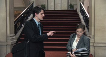 Movie still from “In the Loop” (2009), directed by Armando Iannucci – A man and a woman in business attire on the stairs; Medium shot, Low angle