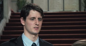 Movie still from “In the Loop” (2009), directed by Armando Iannucci – A man in a suit and tie standing in front of stairs; Close Up shot, Over the shoulder angle