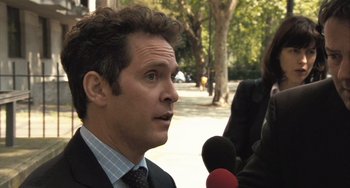 Movie still from “In the Loop” (2009), directed by Armando Iannucci – A man in a suit and tie talking to a microphone; Close Up shot, Over the shoulder angle