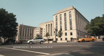 Movie still from “In the Loop” (2009), directed by Armando Iannucci – A car driving down a street next to a large building; Extreme Wide shot, Low angle