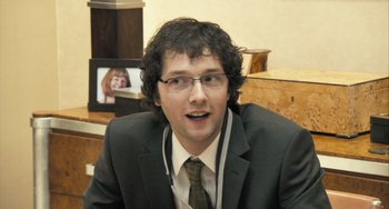 Movie still from “In the Loop” (2009), directed by Armando Iannucci – A man in a suit and tie with glasses; Close Up shot, Over the shoulder angle