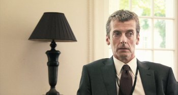 Movie still from “In the Loop” (2009), directed by Armando Iannucci – A man wearing a suit and tie in front of a lamp; Close Up shot, Over the shoulder angle