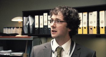 Movie still from “In the Loop” (2009), directed by Armando Iannucci – A man wearing a suit and tie in a room; Close Up shot, Over the shoulder angle