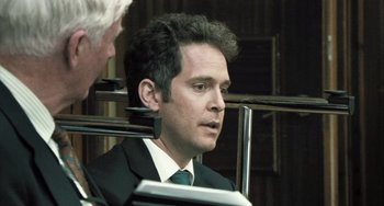 Movie still from “In the Loop” (2009), directed by Armando Iannucci – A person wearing a suit and tie; Close Up shot, Over the shoulder angle
