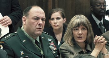 Movie still from “In the Loop” (2009), directed by Armando Iannucci – A man and two women are sitting in front of a wall; Close Up shot, Over the shoulder angle