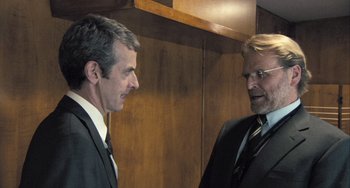 Movie still from “In the Loop” (2009), directed by Armando Iannucci – Two men in business suits talking to each other; Medium shot, Over the shoulder angle