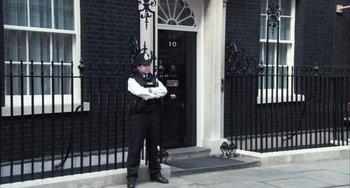 Movie still from “In the Loop” (2009), directed by Armando Iannucci – A police officer standing in front of a building; Wide shot, Low angle