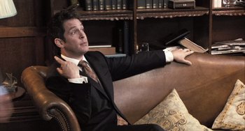 Movie still from “In the Loop” (2009), directed by Armando Iannucci – A man in a suit and tie sitting on top of a couch; Medium shot, Low angle