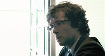 Movie still from “In the Loop” (2009), directed by Armando Iannucci – A person wearing a suit and glasses; Close Up shot, Over the shoulder angle