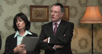 Movie still from “In the Loop” (2009), directed by Armando Iannucci – A man in a suit and tie standing next to a woman in a suit; Medium shot, Over the shoulder angle