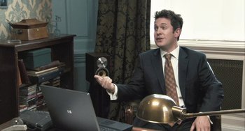 Movie still from “In the Loop” (2009), directed by Armando Iannucci – A man sitting at a desk in front of a computer; Medium shot, High angle
