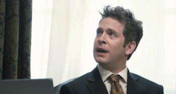 Movie still from “In the Loop” (2009), directed by Armando Iannucci – A person wearing a suit and tie; Close Up shot, Over the shoulder angle