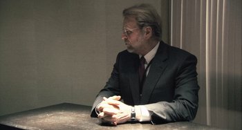 Movie still from “In the Loop” (2009), directed by Armando Iannucci – A man in a suit and tie sitting at a table; Medium shot, Over the shoulder angle