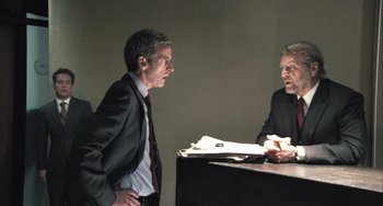 Movie still from “In the Loop” (2009), directed by Armando Iannucci – Two men in business suits talking to each other; Medium shot, Over the shoulder angle