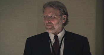 Movie still from “In the Loop” (2009), directed by Armando Iannucci – An older man in a suit and tie looking to his left; Close Up shot, Over the shoulder angle