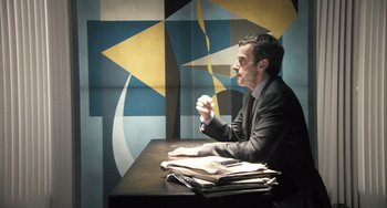 Movie still from “In the Loop” (2009), directed by Armando Iannucci – A man sitting at a table in front of papers; Medium shot, Over the shoulder angle