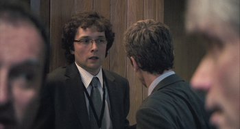 Movie still from “In the Loop” (2009), directed by Armando Iannucci – A man in a suit talking to another man in a suit; Medium shot, Over the shoulder angle