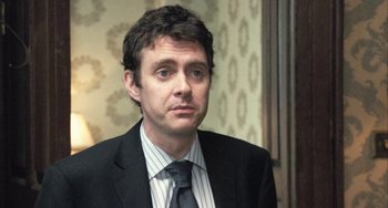 Movie still from “In the Loop” (2009), directed by Armando Iannucci – A person wearing a suit and tie; Close Up shot, Over the shoulder angle