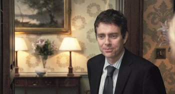 Movie still from “In the Loop” (2009), directed by Armando Iannucci – A man wearing a suit and tie in a room; Medium shot, Over the shoulder angle