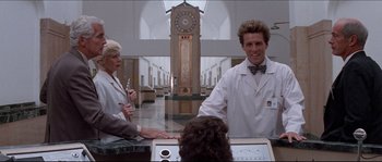 Movie still from “In the Mouth of Madness” (1994), directed by John Carpenter – A man and a woman in white lab coats in front of a clock; Medium shot, Low angle