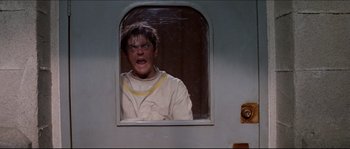 Movie still from “In the Mouth of Madness” (1994), directed by John Carpenter – A man in a white shirt is looking out of a window; Medium shot, Low angle