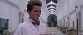 Movie still from “In the Mouth of Madness” (1994), directed by John Carpenter – A man wearing a lab coat and a bow tie; Close Up shot, Low angle