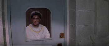 Movie still from “In the Mouth of Madness” (1994), directed by John Carpenter – A man standing in front of a mirror in a room; Medium shot, High angle