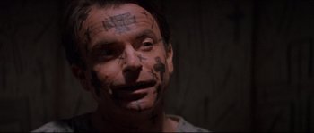 Movie still from “In the Mouth of Madness” (1994), directed by John Carpenter – A man with tattoos on his face and forehead; Close Up shot, High angle
