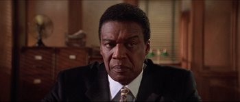 Movie still from “In the Mouth of Madness” (1994), directed by John Carpenter – A man in a suit and a tie; Close Up shot, Low angle