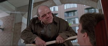 Movie still from “In the Mouth of Madness” (1994), directed by John Carpenter – A bald man holding a baseball bat while wearing a brown jacket; Medium shot, Low angle