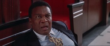 Movie still from “In the Mouth of Madness” (1994), directed by John Carpenter – A man in a suit and tie sitting in a chair; Close Up shot, Low angle