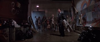 Movie still from “In the Mouth of Madness” (1994), directed by John Carpenter – A group of people standing in a room; Wide shot, Low angle