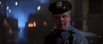 Movie still from “In the Mouth of Madness” (1994), directed by John Carpenter – A police officer with a zombie face on his uniform; Close Up shot, Low angle