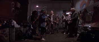Movie still from “In the Mouth of Madness” (1994), directed by John Carpenter – A group of people dressed in costumes and holding axes; Wide shot, Low angle