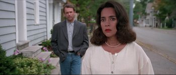 Movie still from “In the Mouth of Madness” (1994), directed by John Carpenter – A man and a woman standing next to each other; Close Up shot, Over the shoulder angle