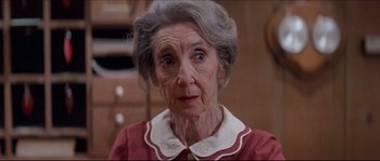 Movie still from “In the Mouth of Madness” (1994), directed by John Carpenter – An older woman with a white collar looking at the camera; Close Up shot, Low angle