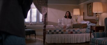 Movie still from “In the Mouth of Madness” (1994), directed by John Carpenter – A woman sitting on top of a bed in a bedroom; Wide shot, High angle