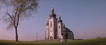 Movie still from “In the Mouth of Madness” (1994), directed by John Carpenter – Two people are standing in front of a large church; Extreme Wide shot, Low angle