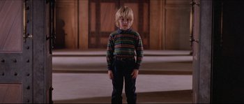 Movie still from “In the Mouth of Madness” (1994), directed by John Carpenter – A young boy standing in front of a wooden wall; Medium shot, Low angle