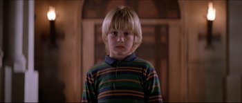 Movie still from “In the Mouth of Madness” (1994), directed by John Carpenter – A young boy with blonde hair wearing a striped shirt; Close Up shot, Low angle
