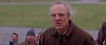 Movie still from “In the Mouth of Madness” (1994), directed by John Carpenter – An older man with a long white hair and a brown jacket; Close Up shot, Low angle