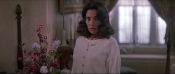 Movie still from “In the Mouth of Madness” (1994), directed by John Carpenter – A woman in a white shirt is standing in a room; Close Up shot, Over the shoulder angle