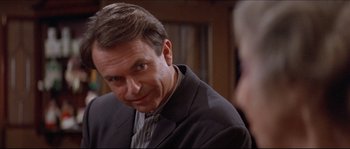 Movie still from “In the Mouth of Madness” (1994), directed by John Carpenter – A person wearing a suit and tie; Close Up shot, Over the shoulder angle