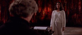 Movie still from “In the Mouth of Madness” (1994), directed by John Carpenter – A woman standing in front of an old fashioned typewriter; Medium shot, Over the shoulder angle